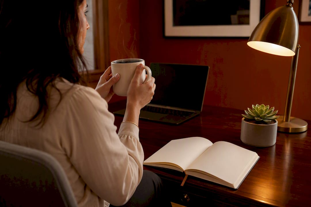 Hands holding coffee near blank notebook